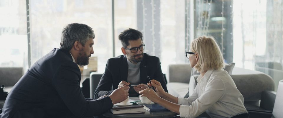 Tre persone in conversazione attorno a un tavolino, accanto a una grande vetrata